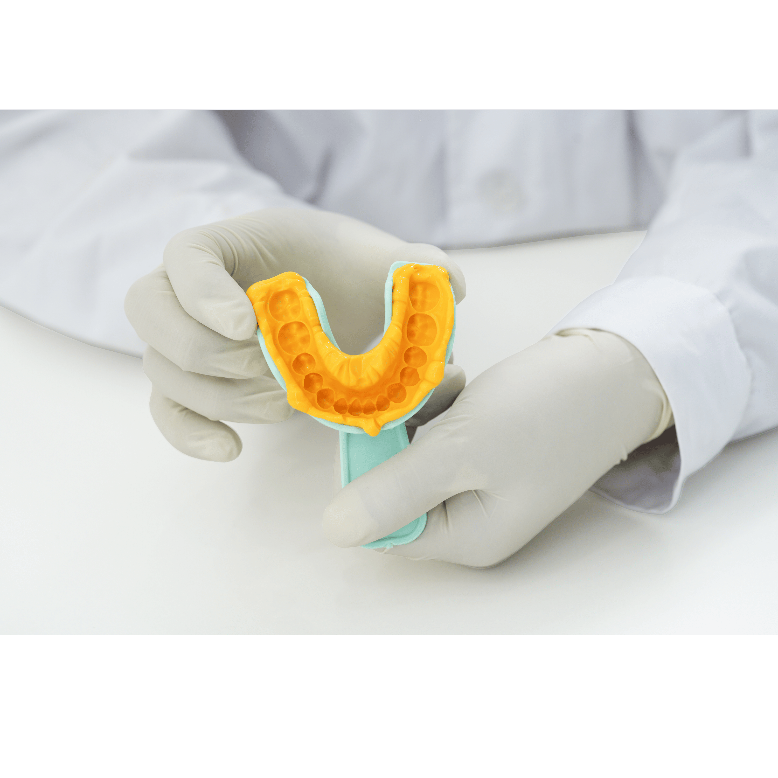 Person wearing gloves holding a dental impression tray with an orange impression in a white background